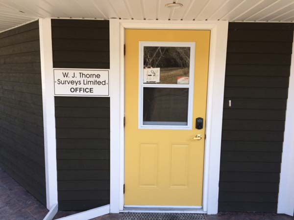 Front entrance of the W. J. Thorne Surveys Limited office at 298 River Road, Blaketown — a yellow door with the office sign on dark grey siding